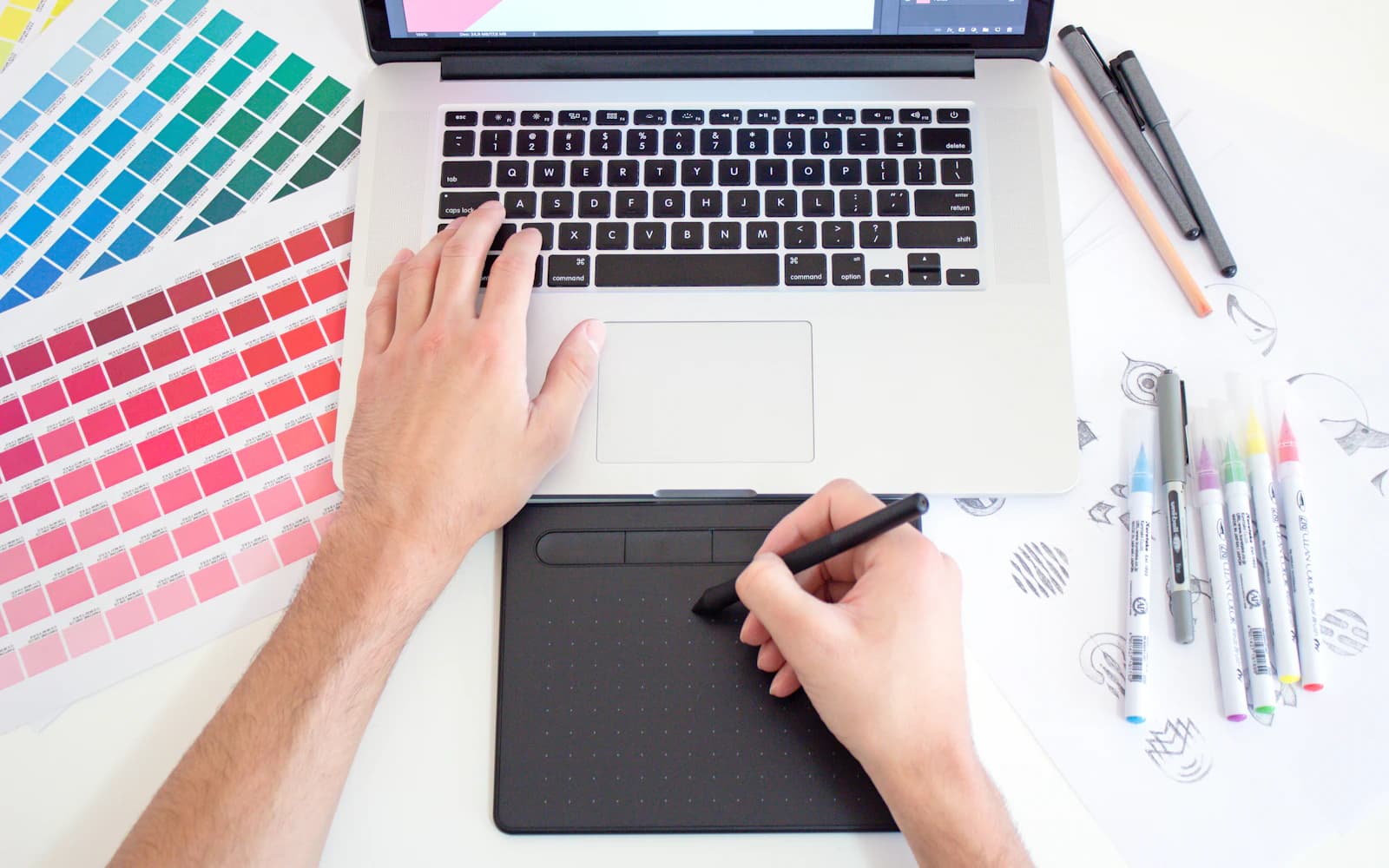 Designer sketching on a drawing tablet beside colour swatches